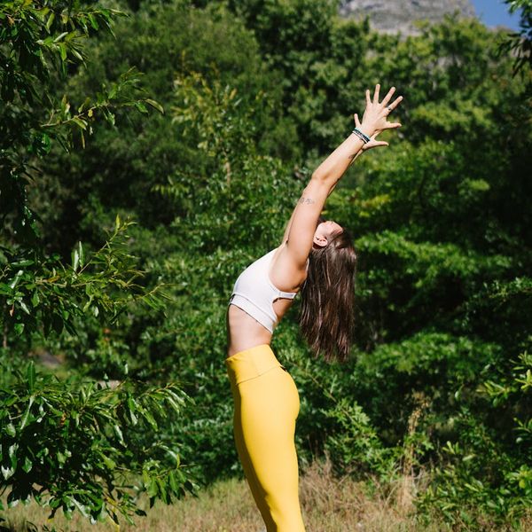 Woman practicing a yoga pose in a green forest with sun rays.